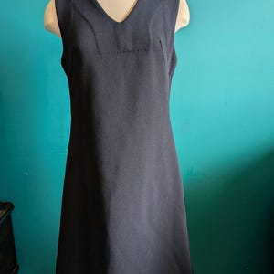 May include: A sleeveless black dress with a v-neckline. The dress is made of a textured fabric and has a simple, classic design.