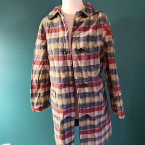 May include: A long-sleeved plaid coat with a button closure. The coat is made of a lightweight fabric and has a relaxed fit. The plaid pattern is in shades of red, blue, green, and yellow.