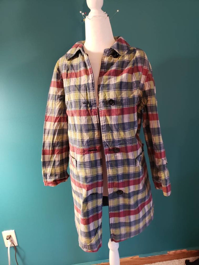May include: A long-sleeved plaid coat with a button closure. The coat is made of a lightweight fabric and has a relaxed fit. The plaid pattern is in shades of red, blue, green, and yellow.