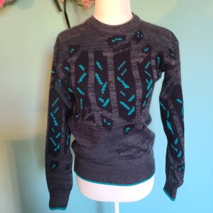 May include: A gray and teal patterned sweater with a crew neck. The sweater has a geometric design with teal accents.