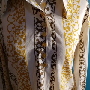 May include: A white button-down shirt with brown and gold vertical stripes and a floral pattern. The shirt has a pointed collar and long sleeves.