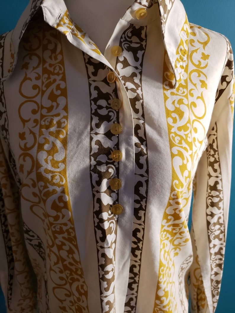May include: A white button-down shirt with brown and gold vertical stripes and a floral pattern. The shirt has a pointed collar and long sleeves.