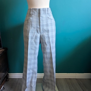 May include: Light blue and gray plaid trousers with a high waist and wide leg. The pants are displayed on a mannequin. The plaid pattern is a classic design, suitable for various occasions. The trousers are made of a medium-weight fabric.