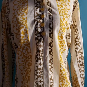 May include: A white button-down shirt with vertical stripes in brown and yellow. The stripes feature a repeating pattern of stylized floral designs.
