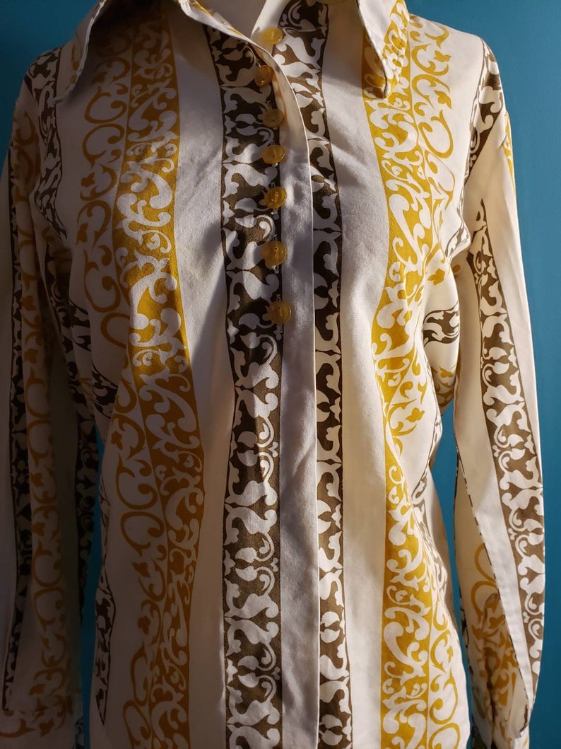 May include: A white button-down shirt with vertical stripes in brown and yellow. The stripes feature a repeating pattern of stylized floral designs.