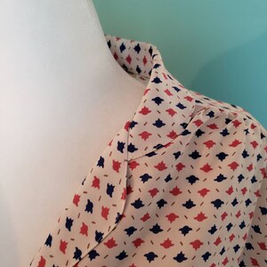 May include: A close-up of the collar of a cream-colored blouse with a red and navy blue geometric pattern.