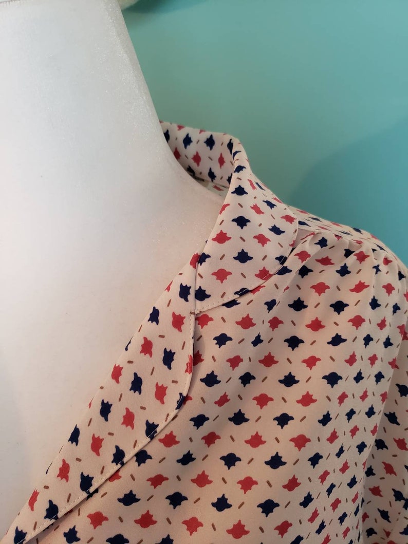 May include: A close-up of the collar of a cream-colored blouse with a red and navy blue geometric pattern.