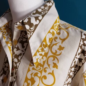 May include: A white button-down shirt with a brown and yellow patterned design. The pattern features a repeating design of stylized floral motifs.