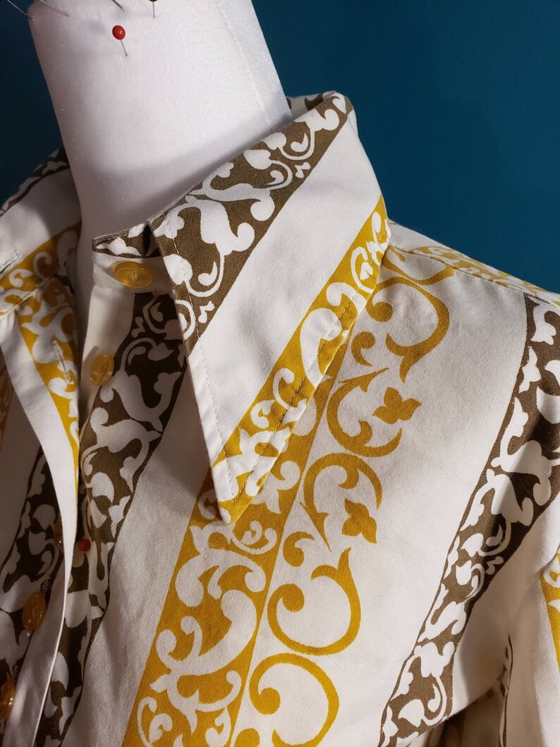 May include: A white button-down shirt with a brown and yellow patterned design. The pattern features a repeating design of stylized floral motifs.