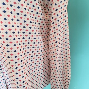 May include: A white long-sleeved shirt with a repeating pattern of small red, blue, and gold shapes.