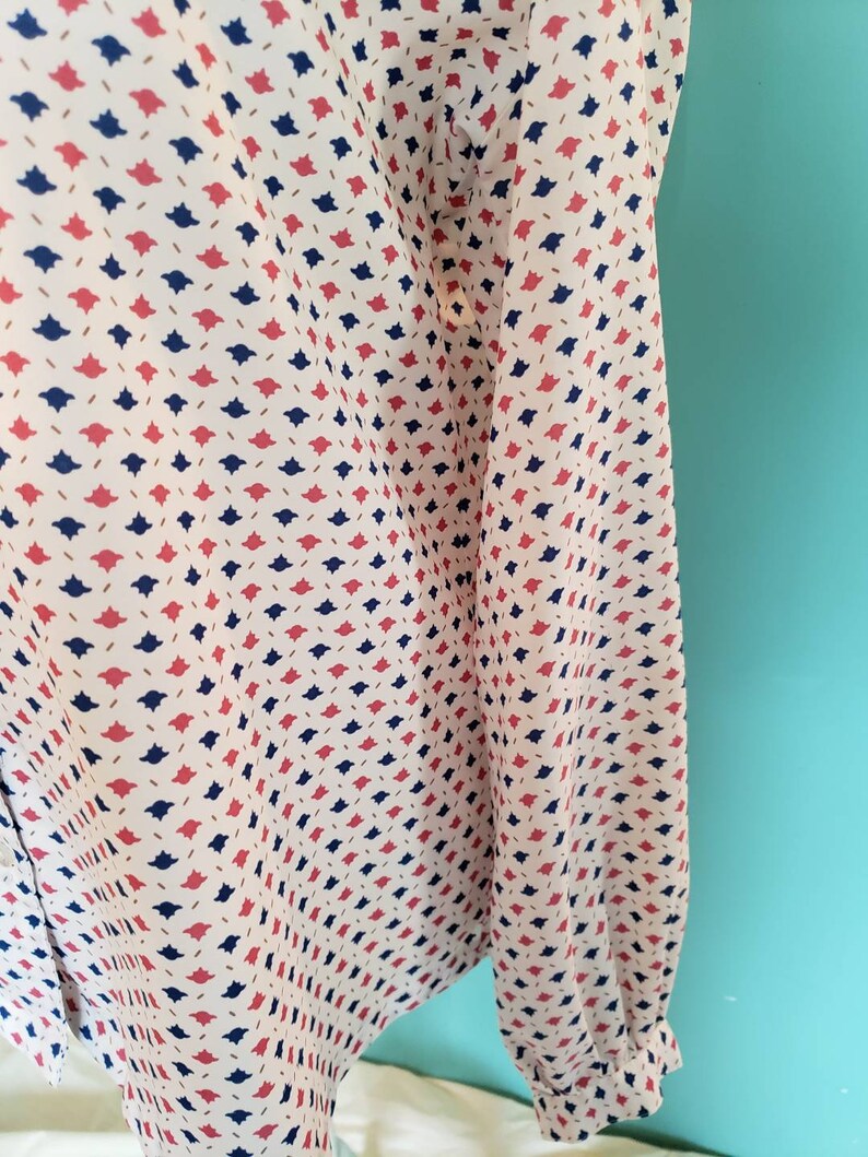 May include: A white long-sleeved shirt with a repeating pattern of small red, blue, and gold shapes.