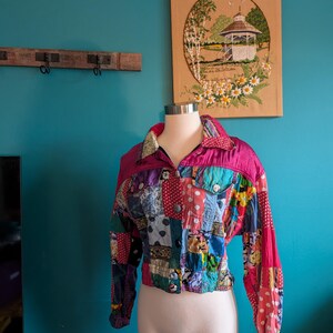 May include: A patchwork jacket with a vibrant mix of colors and patterns. The jacket features a magenta collar and sleeves, with a variety of fabric squares in different colors and designs. The jacket is displayed on a mannequin.