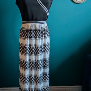 May include: A vintage black and white maxi dress on a mannequin. The top is black with white trim, and the skirt features a repeating black and white checkered pattern. The dress is floor-length and appears to be made of a knit fabric. The dress is displayed indoors.