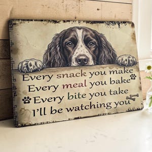 May include: A rectangular metal sign featuring a brown and white spaniel dog peering over a ledge. The text reads: Every snack you make, Every meal you bake, Every bite you take, I'll be watching you. The design includes small paw print icons.