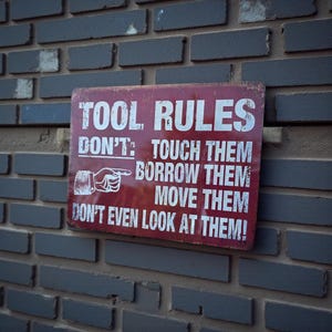 A distressed red metal sign with white text reading TOOL RULES mounted on a grey brick wall.