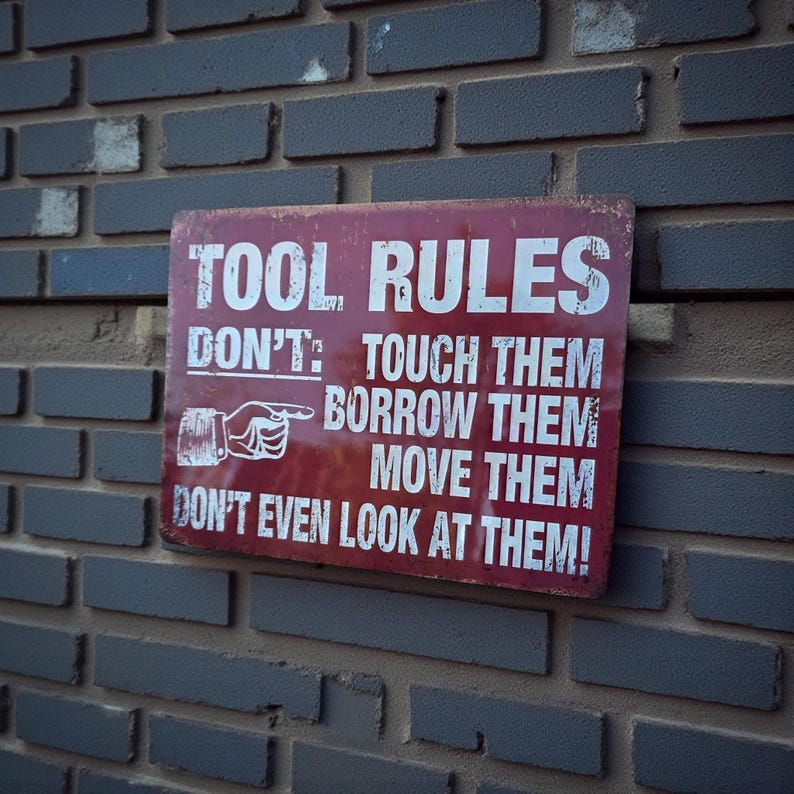 A distressed red metal sign with white text reading TOOL RULES mounted on a grey brick wall.