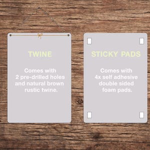 May include: Two rectangular, light gray signs with rounded corners are displayed against a wooden background. The left sign reads "TWINE" and includes text about pre-drilled holes and twine. The right sign reads "STICKY PADS" and includes text about self-adhesive foam pads.