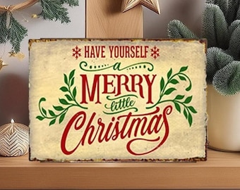 May include: A rectangular metal sign with a distressed cream background featuring the red and green text "HAVE YOURSELF a MERRY little CHRISTMAS" accented with green leafy flourishes and red snowflake symbols at the top of the design.