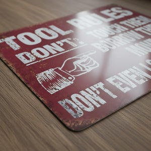 Close-up detail shot of the high-gloss aluminum Tool Rules sign on a wooden workbench.