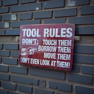 A distressed red metal sign with white text reading TOOL RULES mounted on a grey brick wall.