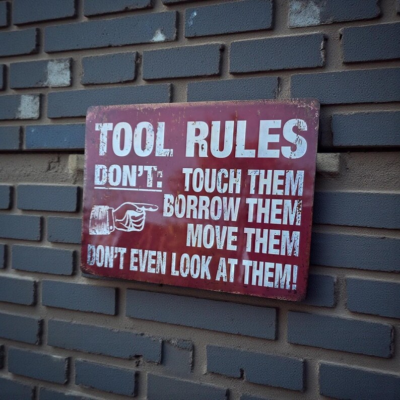A distressed red metal sign with white text reading TOOL RULES mounted on a grey brick wall.