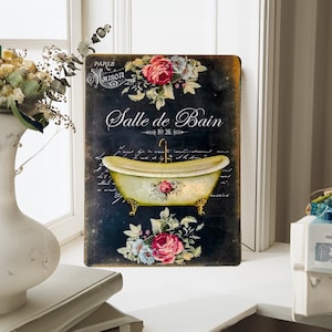 May include: A vintage-style metal sign with a black background and white text that reads "Salle de Bain" with a floral design and a bathtub illustration. The sign is ideal for a bathroom or powder room.