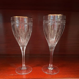 May include: Two clear glass wine glasses with a gold rim and a cut crystal design.