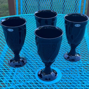 May include: Four black glass goblets with a textured design and a clear glass base. The goblets are on a blue metal table.