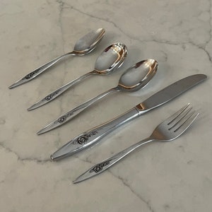 May include: A set of five silver-toned flatware pieces with a rose design. The set includes a fork, knife, and three spoons.