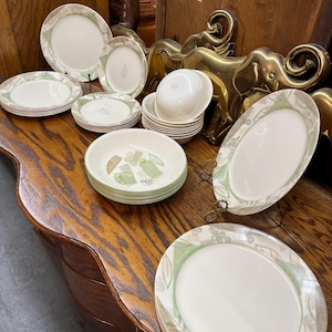 May include: A collection of vintage dinnerware featuring white plates and bowls with a green and tan floral leaf design. The set includes various sizes of plates and bowls, perfect for a complete dining experience.
