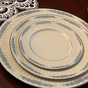 May include: Set of four white ceramic dinner plates with a blue and silver floral design. The plates are nested inside each other.