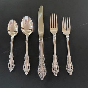 May include: Five pieces of silverware, including a knife, two spoons, and two forks, all with ornate handles. The silverware is made of polished stainless steel.