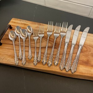 May include: A set of silverware with ornate handles, including forks, spoons, and knives. The silverware is arranged on a wooden surface.