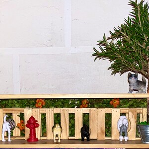 May include: A wooden shelf with a miniature fence and green moss. There are miniature figurines of dogs and a fire hydrant. A small potted plant sits on the shelf.