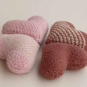 May include: Two knitted heart-shaped pillows, one pink with white stripes and one brown with white stripes.