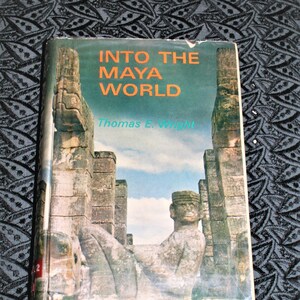 Puede incluir: Un libro antiguo de tapa dura titulado "Into the Maya World" de Thomas E. Wright. La portada presenta una fotografía de antiguas ruinas mayas con una escultura de piedra en primer plano.