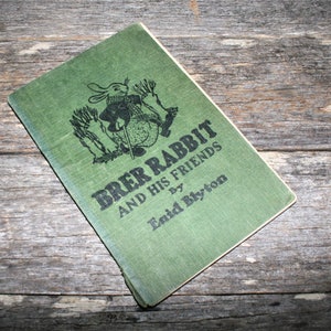 May include: A green book titled "BRER RABBIT AND HIS FRIENDS" by Enid Blyton. The cover features a black and white illustration of a rabbit holding a stick.