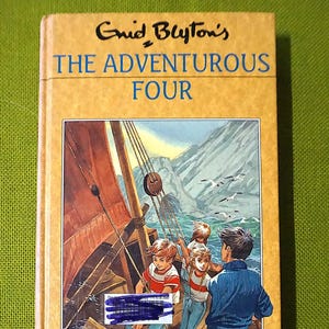 May include: A vintage copy of "Enid Blyton's The Adventurous Four" with a tan cover and blue lettering. The cover illustration depicts children on a sailing boat. The book is a classic children's story.