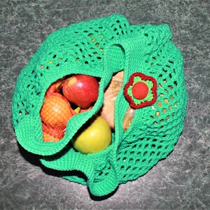 May include: Green crocheted mesh bag with a red flower embellishment, filled with apples, oranges, and a pear.
