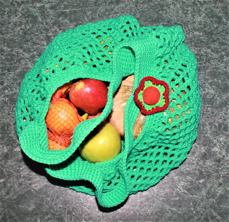 May include: Green crocheted mesh bag with a red flower embellishment, filled with apples, oranges, and a pear.