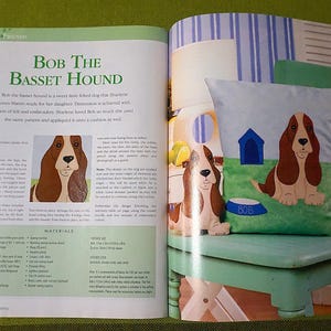 Puede incluir: Una p&aacute;gina de revista con el t&iacute;tulo "BOB THE BASSET HOUND". Presenta un coj&iacute;n con un dise&ntilde;o de Basset Hound, una caseta para perros y un cuenco para comida en un banco verde. El perro es marr&oacute;n y blanco. El texto incluye la palabra "MATERIALES".