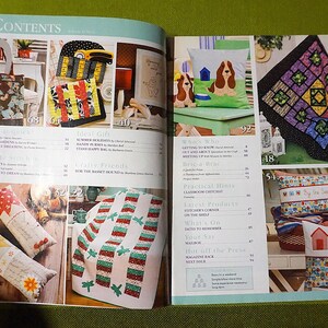 Puede incluir: P&aacute;gina doble abierta de una revista de manualidades. Muestra varios art&iacute;culos hechos a mano, incluyendo un bolso de mano, edredones, cojines con motivos de perros y casas, y una colcha de retazos. La p&aacute;gina de "Contenidos" es visible.