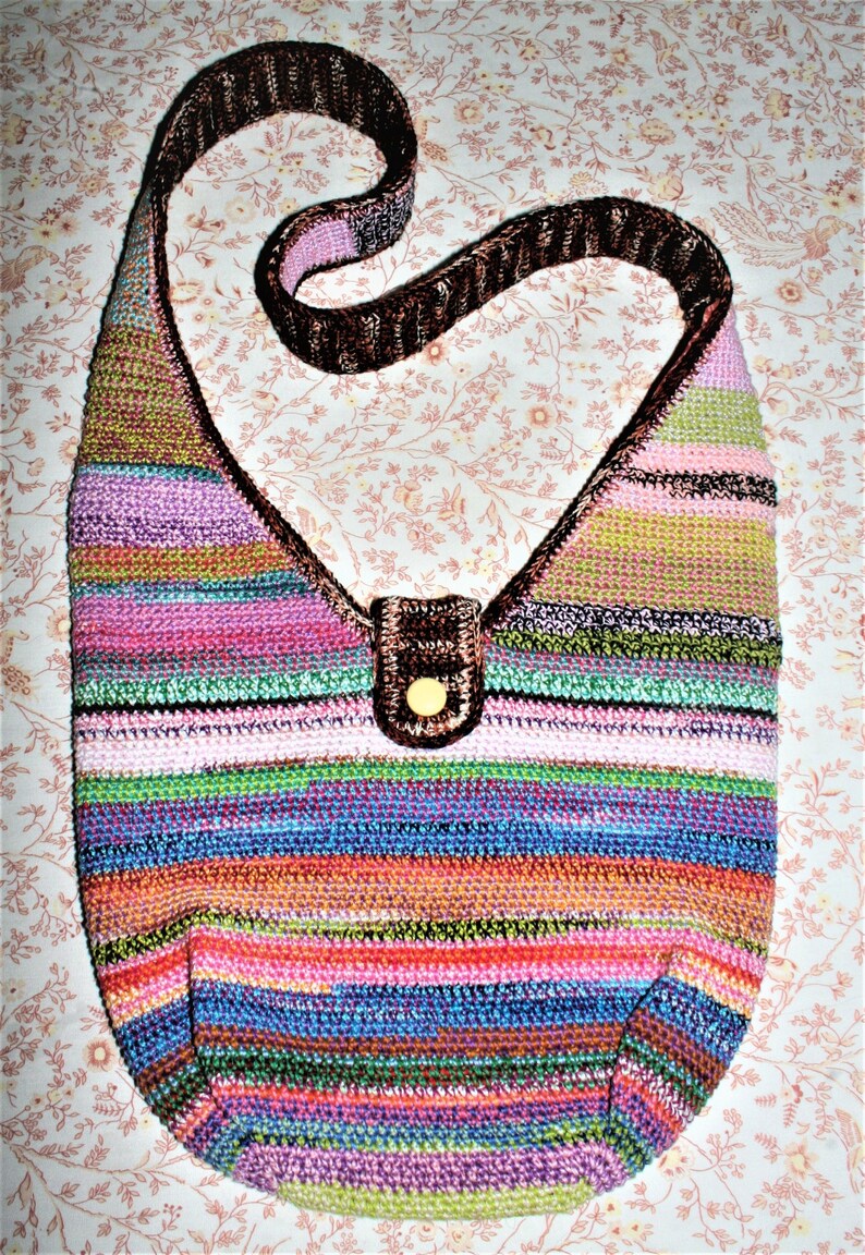 K&ouml;nnte beinhalten: Eine mehrfarbige gestreifte geh&auml;kelte Schultertasche mit einem braunen Lederriemen und einem braunen Knopfverschluss.