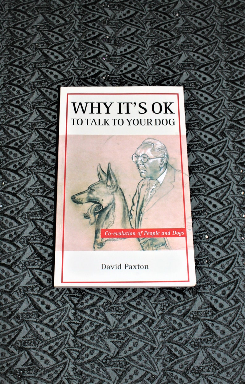 May include: A white book cover with the title "WHY IT'S OK TO TALK TO YOUR DOG" in black text. The cover features a black and white illustration of a man and a dog. The text "Co-evolution of People and Dogs" is in red text below the illustration. The author's name, "David Paxton", is in black text at the bottom of the cover.