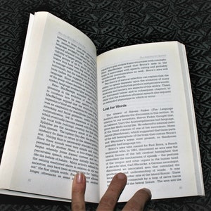 May include: A close-up of an open book with a finger pointing to a section titled "Lost for Words". The text discusses the evolution of language and the role of specific brain areas, including Broca's area and Wernicke's area, in speech.