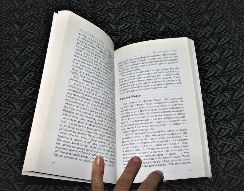 May include: A close-up of an open book with a finger pointing to a section titled "Lost for Words". The text discusses the evolution of language and the role of specific brain areas, including Broca's area and Wernicke's area, in speech.