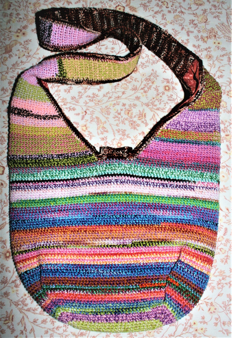 K&ouml;nnte beinhalten: Eine bunte gestreifte geh&auml;kelte Umh&auml;ngetasche mit einem braunen Riemen. Die Tasche ist aus verschiedenen Farben gefertigt, darunter Pink, Gr&uuml;n, Blau und Orange.