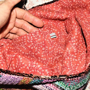 K&ouml;nnte beinhalten: Eine geh&auml;kelte Tasche mit einem bunten Patchwork-Design. Das Innere der Tasche ist mit einem roten Stoff mit einem wei&szlig;en Blumenmuster ausgekleidet.