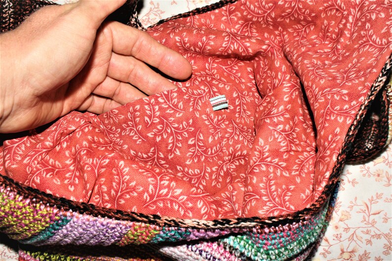 K&ouml;nnte beinhalten: Eine geh&auml;kelte Tasche mit einem bunten Patchwork-Design. Das Innere der Tasche ist mit einem roten Stoff mit einem wei&szlig;en Blumenmuster ausgekleidet.