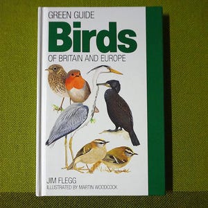 May include: A hardcover book titled "Birds of Britain and Europe" with illustrations of various bird species. The cover features a green spine and a white front with the title in large green letters. The book is by Jim Flegg and illustrated by Martin Woodcock.